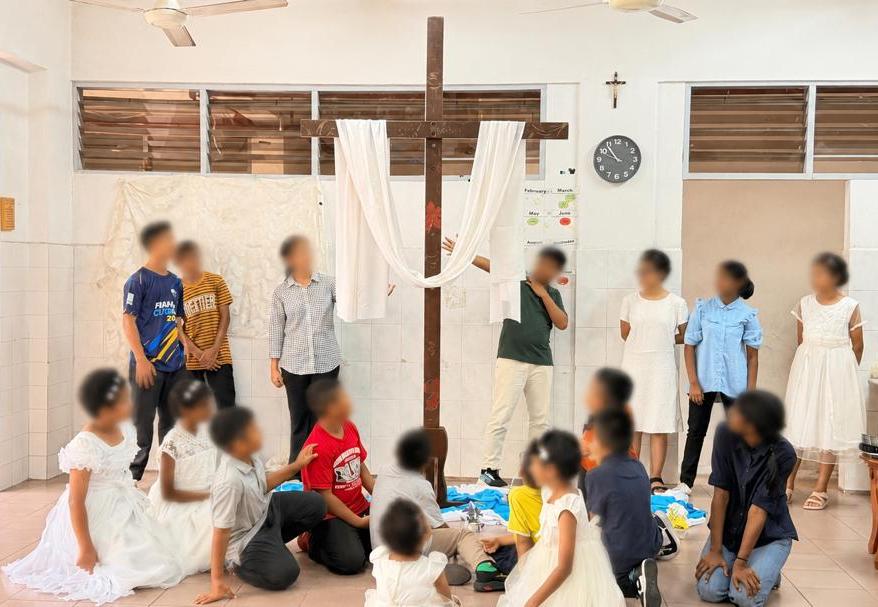 Children of St Joseph's Home gathered around the wooden cross during Perjalanan Salib